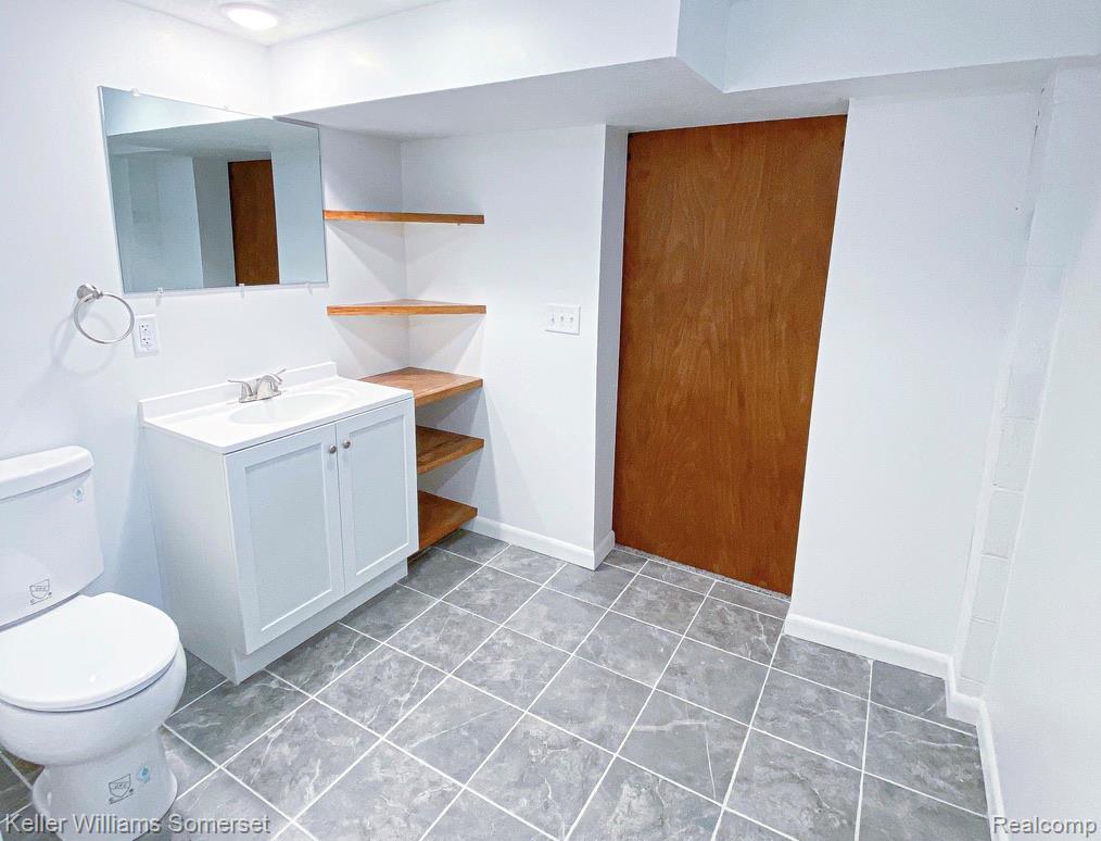 1821 Nazareth Road Kalamazoo, MI 49048 - Photo 17 of 20 Bathroom featuring a white vanity with integrated sink, rectangular mirror, corner shelving, and gray square floor tiles