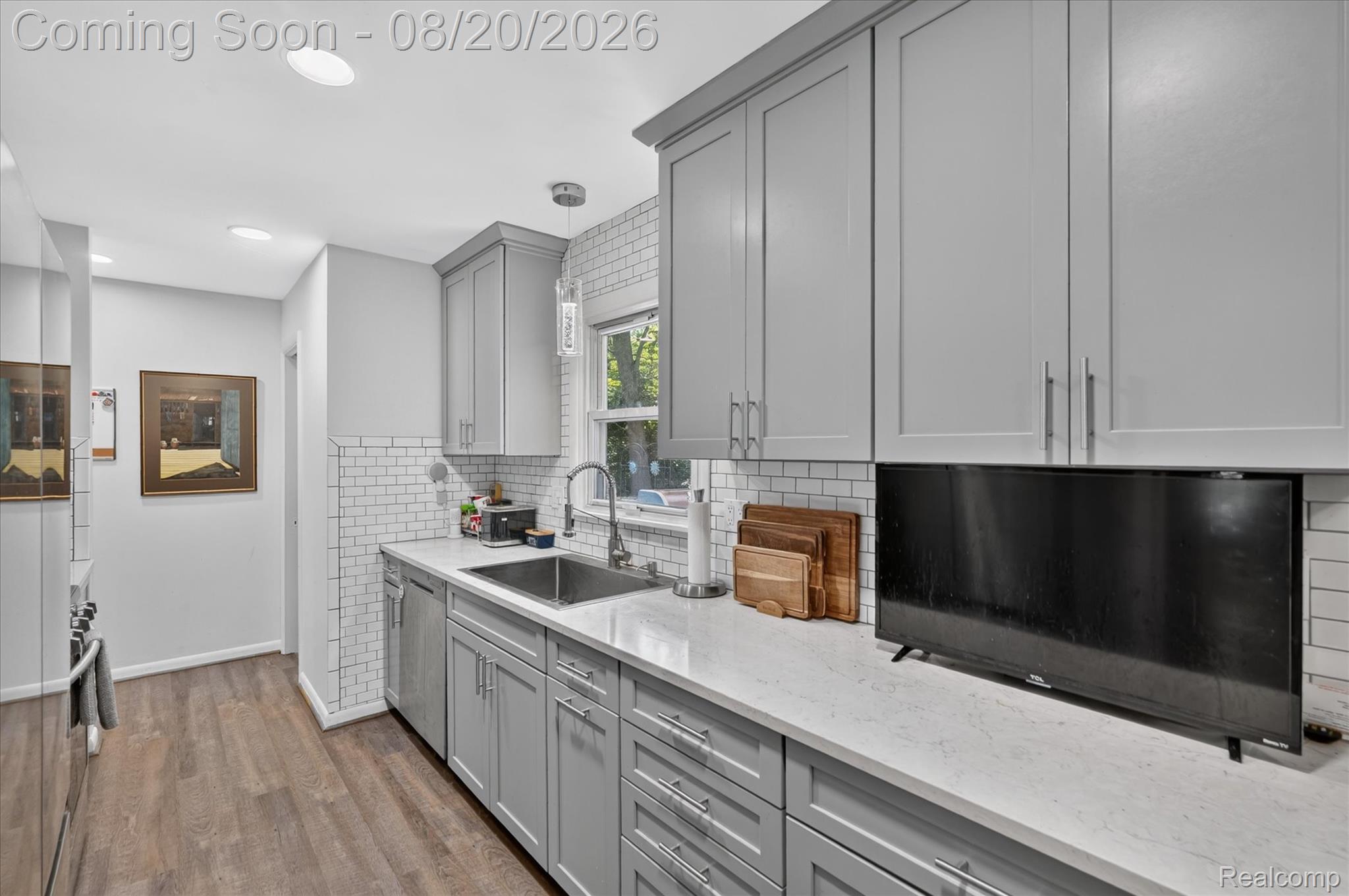 6235 Waldon Road Clarkston, MI 48346 - Photo 6 of 41 Light gray shaker-style cabinetry, stainless steel sink, white subway tile backsplash, light-toned countertops, and wood-finish flooring