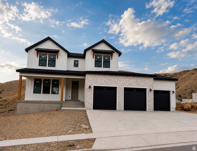 5885 Canyon Rim Road, Unit 624 Lehi, UT 84048 - Photo 1 of 10 Modern farmhouse-style exterior featuring white vertical and horizontal siding, a three-car garage with black doors, light stone veneer accents, and a covered porch with natural wood posts