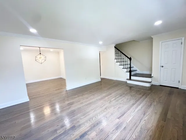 a view of an empty room with wooden floor and stairs