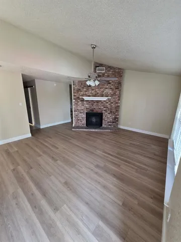 a view of an empty room with wooden floor fireplace and a window