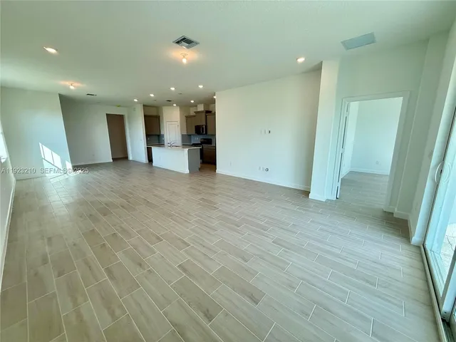 an empty room with wooden floor kitchen and windows