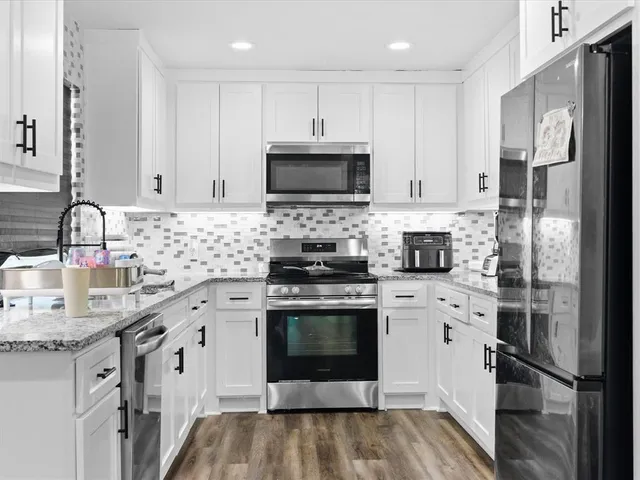 a kitchen with stainless steel appliances granite countertop a refrigerator stove a sink and white cabinets