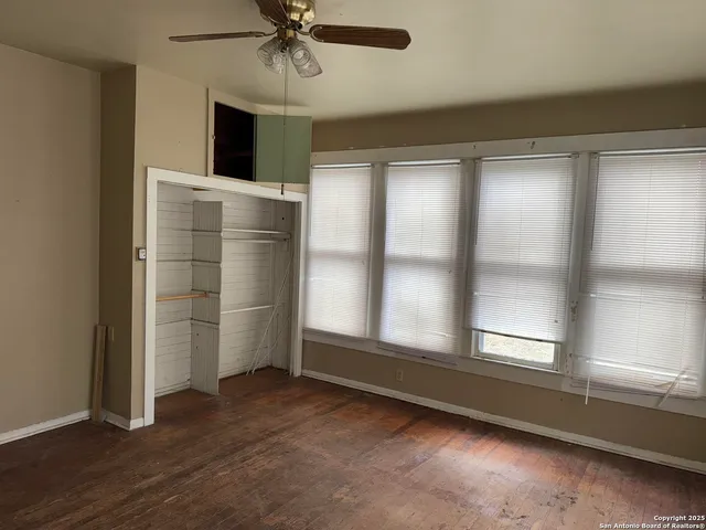 an empty room with wooden floor fan and windows