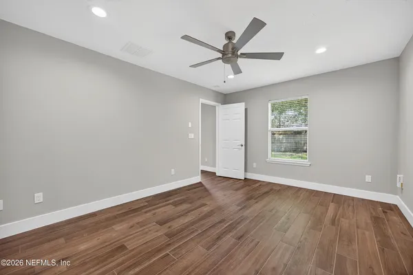 an empty room with wooden floor fan and windows