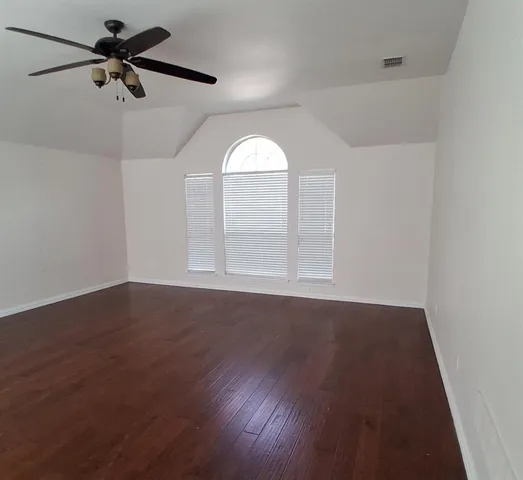 an empty room with wooden floor fan and windows