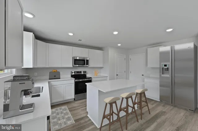 a kitchen with stainless steel appliances granite countertop a stove a sink a refrigerator white cabinets and couches with wooden floor