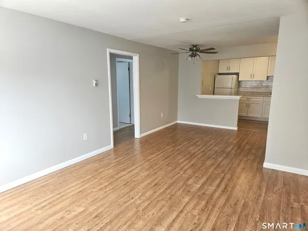 a view of empty room with wooden floor and kitchen