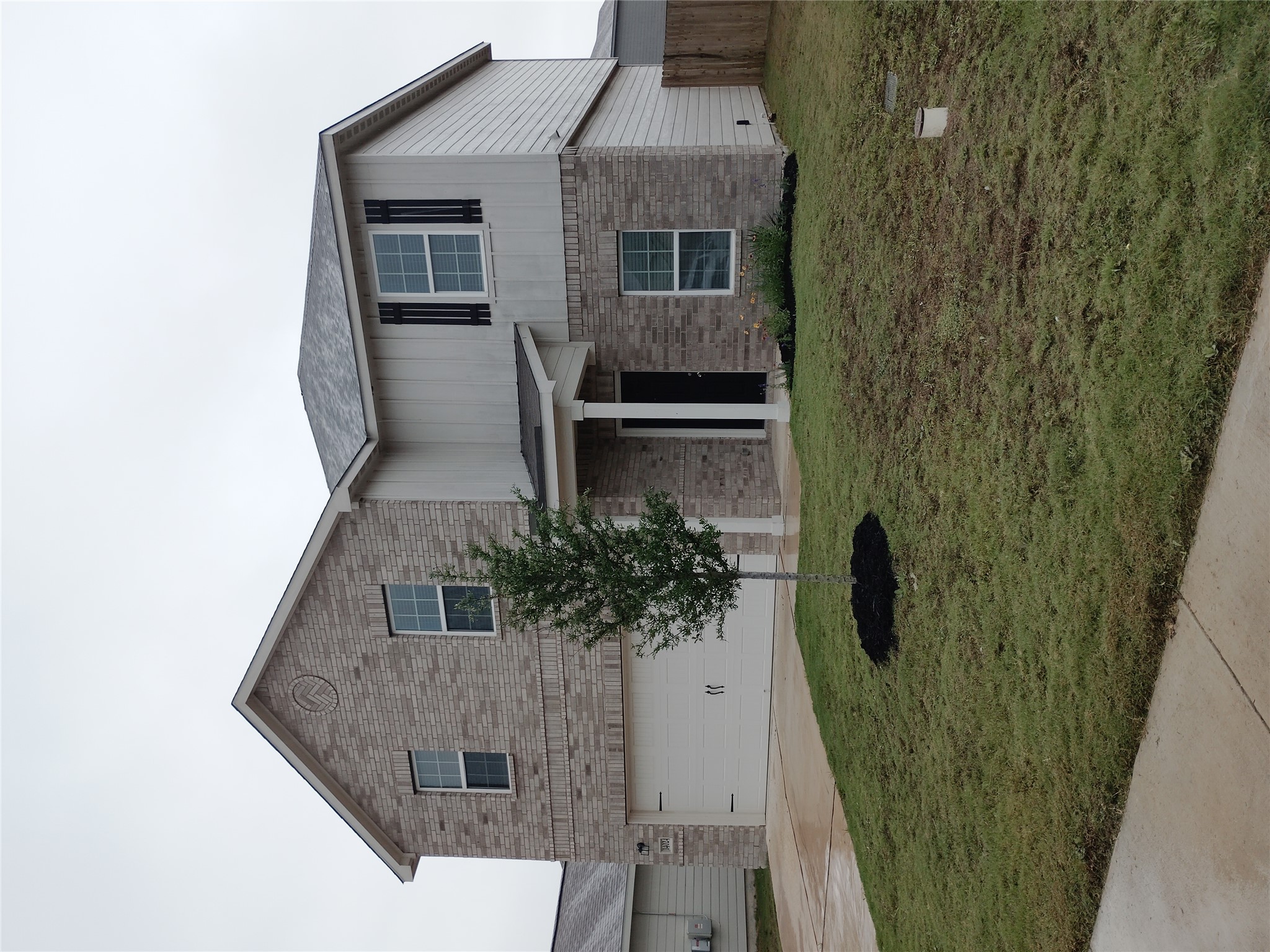 14024 Prairie Schooner Pass Elgin, TX 78621 - Photo 2 of 20 Two-story residence featuring brick and siding exterior, an attached garage, covered entryway, and a landscaped front yard with a young tree