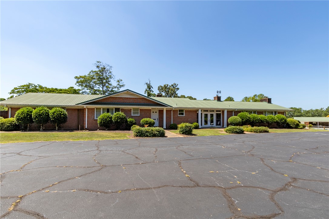 1302 Leeward Road Anderson, SC 29625 - Photo 45 of 50 A sprawling brick building with a vivid green metal roof, set against a clear blue sky, offers a vast parking area.