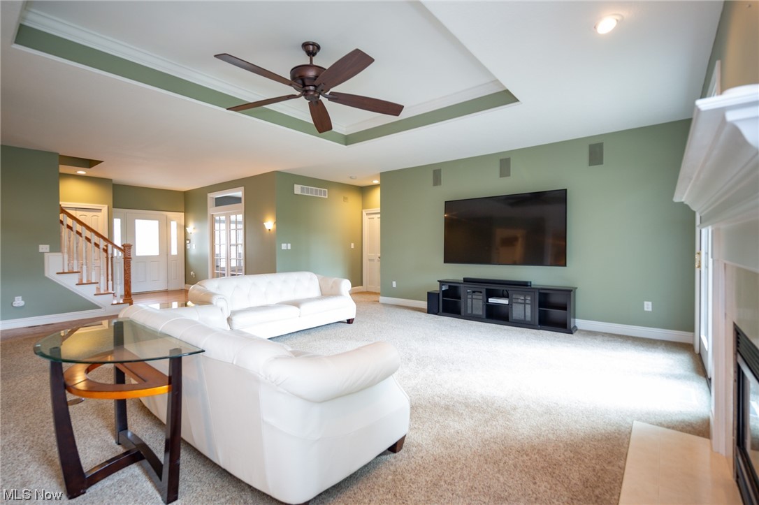 Living room featuring a raised ceiling, ceiling fan, light carpet, and ornamental molding