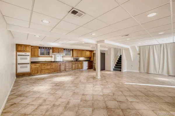 a view of an empty room with kitchen and window