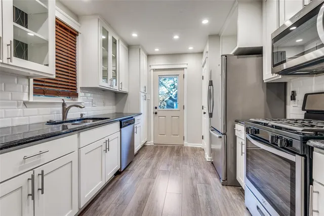 a kitchen with stainless steel appliances granite countertop a stove a sink dishwasher a refrigerator and white cabinets with wooden floor