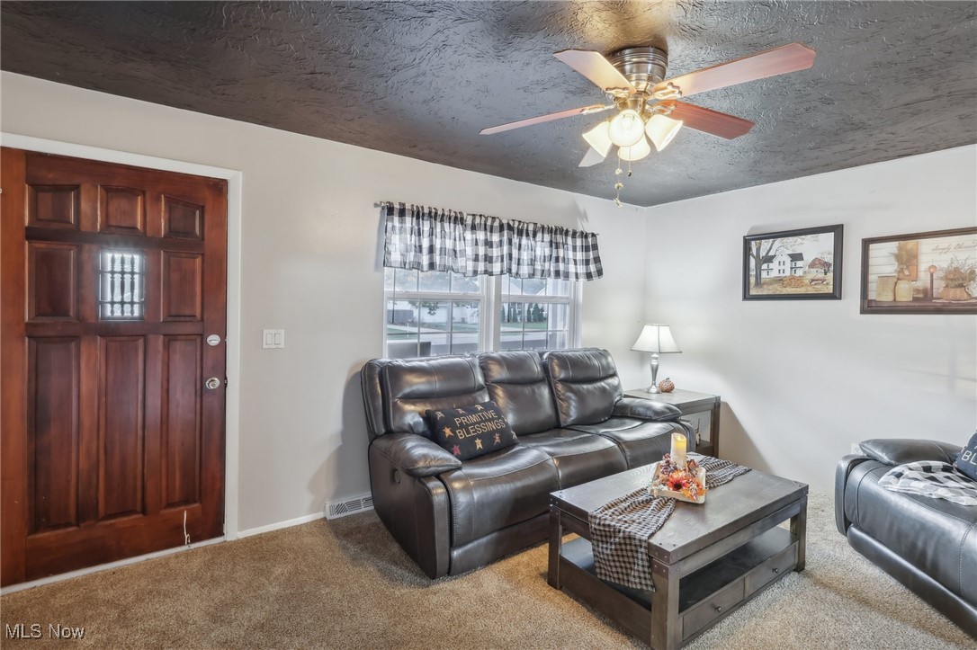 Living room with a textured ceiling, light carpet, and ceiling fan