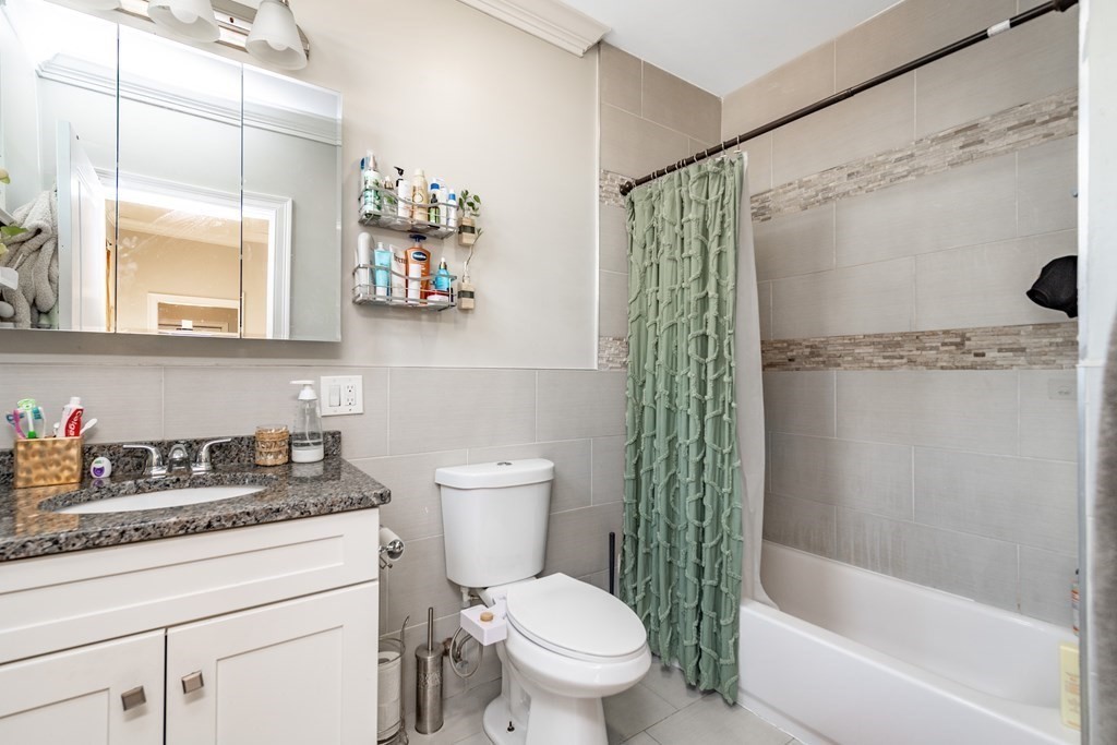 50-52 Townsend Street Boston, MA 02119 - Photo 9 of 15 a bathroom with a granite countertop sink a toilet a mirror a bathtub and shower