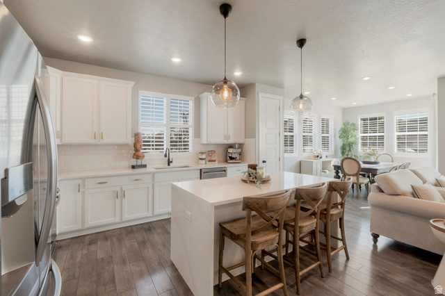 2319 North 3370 West Lehi, UT 84048 - Photo 7 of 30 Open-concept kitchen featuring white shaker cabinetry, stainless steel appliances, a center island with countertop seating, wood-finish flooring, and recessed lighting