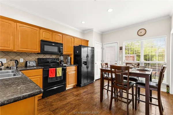 a kitchen with stainless steel appliances granite countertop a stove top oven a sink a dining table and chairs with wooden floor