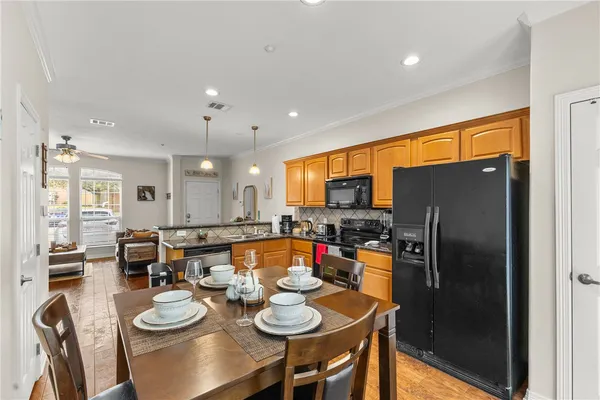 a kitchen with stainless steel appliances granite countertop a refrigerator a sink a stove a dining table and chairs with wooden floor