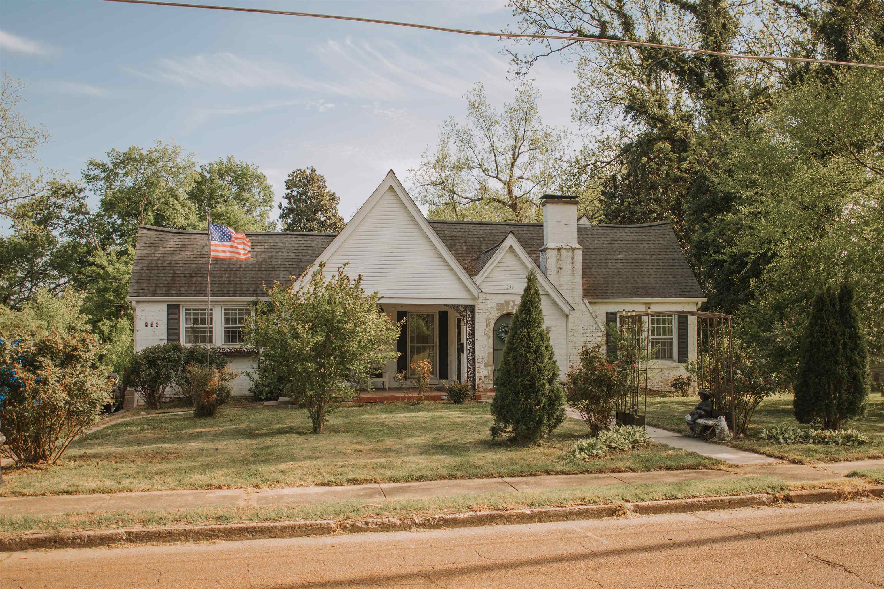 Tudor house featuring covered porch, a front lawn, a chimney, and roof with shingles