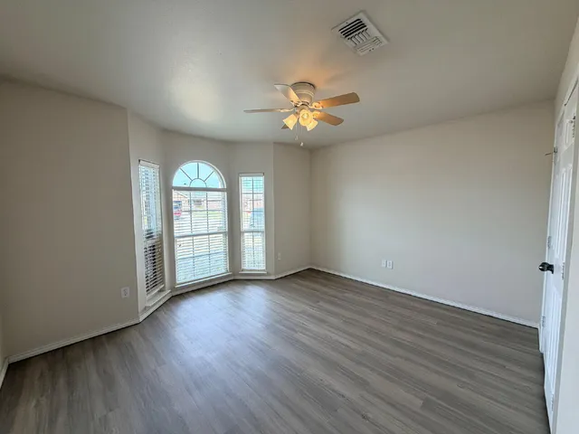 an empty room with wooden floor fan and windows