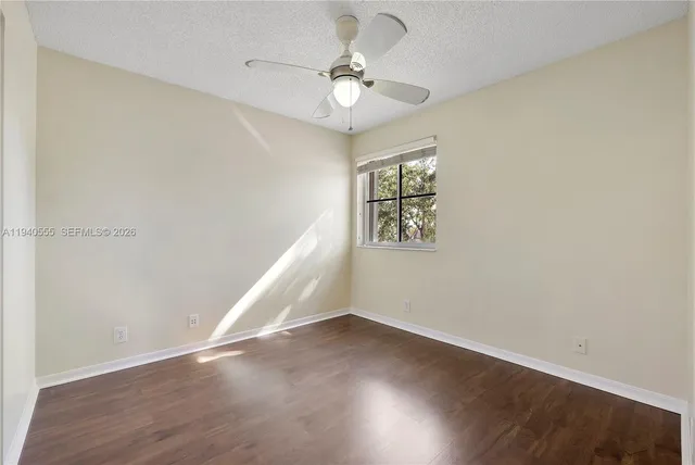 an empty room with wooden floor chandelier fan and windows