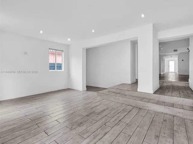 a view of an empty room with wooden floor and a bathroom