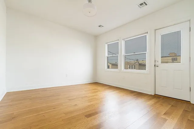 a view of an empty room with window and wooden floor
