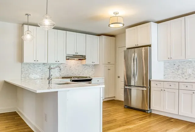 a kitchen with granite countertop a refrigerator a sink and white cabinets