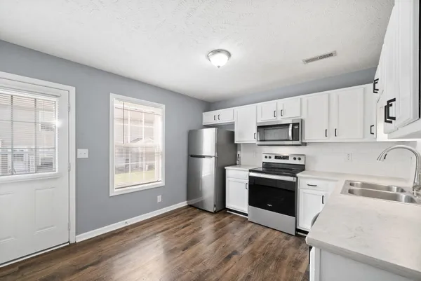 a kitchen with stainless steel appliances granite countertop a stove a sink dishwasher a refrigerator and a microwave oven with white cabinets