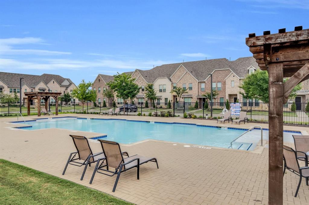 1498 Weston Road Dallas, TX 75234 - Photo 24 of 24 Community swimming pool with a paved deck, surrounded by townhomes featuring brick and siding exteriors, enclosed by a black metal fence, and accented by mature landscaping