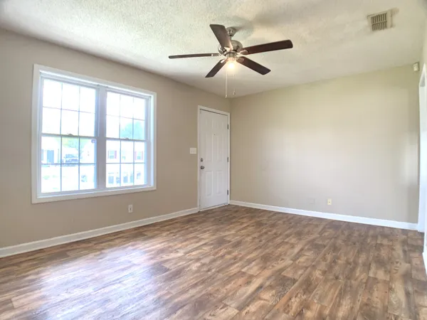 an empty room with wooden floor fan and windows
