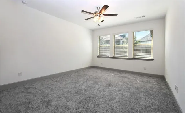 an empty room with chandelier fan and windows