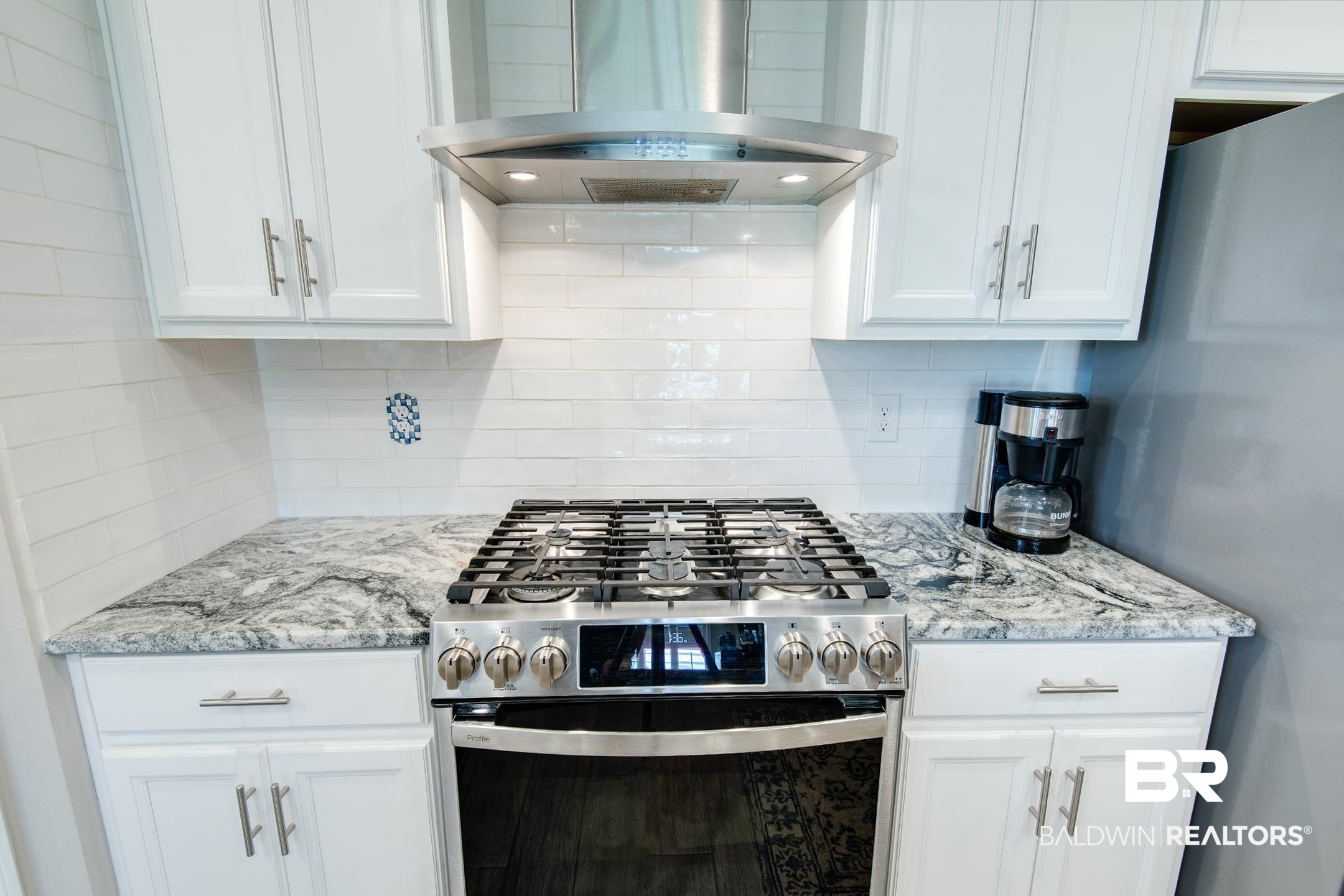 9988 Dunleith Loop Daphne, AL 36526 - Photo 34 of 51 Kitchen featuring wall chimney range hood, backsplash, white cabinetry, and appliances with stainless steel finishes