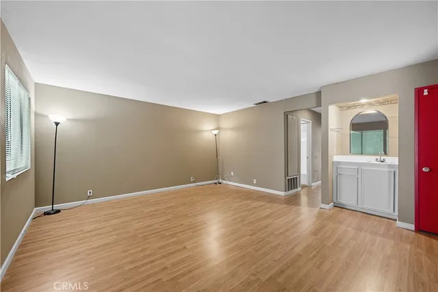 a view of an empty room with wooden floor and a kitchen