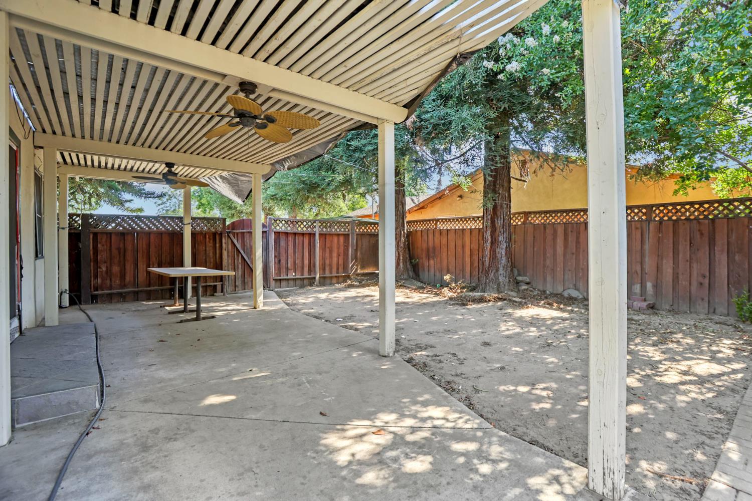 916 Elm Avenue Modesto, CA 95351 - Photo 32 of 52 Covered patio area with concrete surface, ceiling fans, mature tree shade, and private fenced yard space.