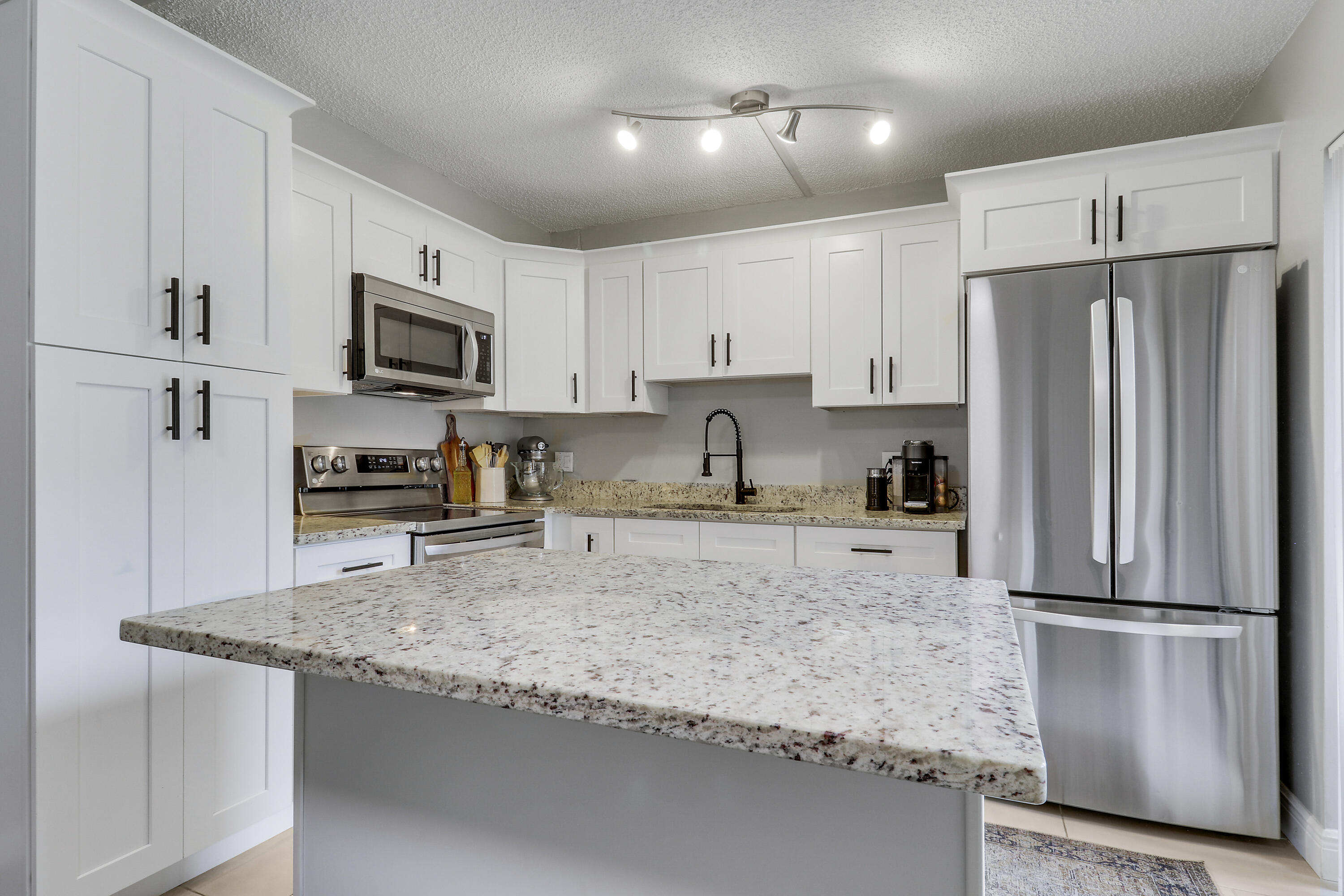 187 Woodland Road Palm Springs, FL 33461 - Photo 6 of 29 a kitchen with granite countertop a refrigerator a sink a stove a microwave and cabinets