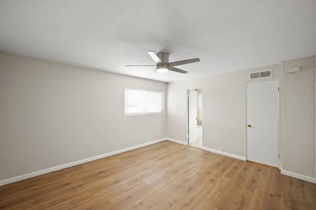 an empty room with wooden floor ceiling fan and windows