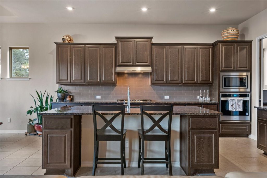 6705 Destination Way Jonestown, TX 78645 - Photo 9 of 39 Rich, espresso-toned cabinetry provides a stunning contrast against the neutral tile, anchored by a large island that’s ready for morning coffee or evening hors d'oeuvres.