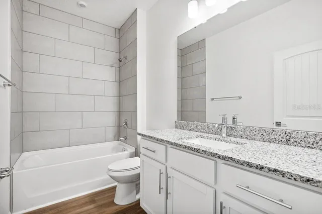 a bathroom with a granite countertop bathtub shower sink vanity and toilet