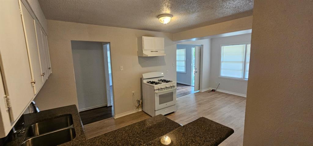 5170 Cardiff Street Dallas, TX 75241 - Photo 2 of 14 Kitchen featuring white gas range oven, wood finished floors, under cabinet range hood, white cabinetry, and a textured ceiling