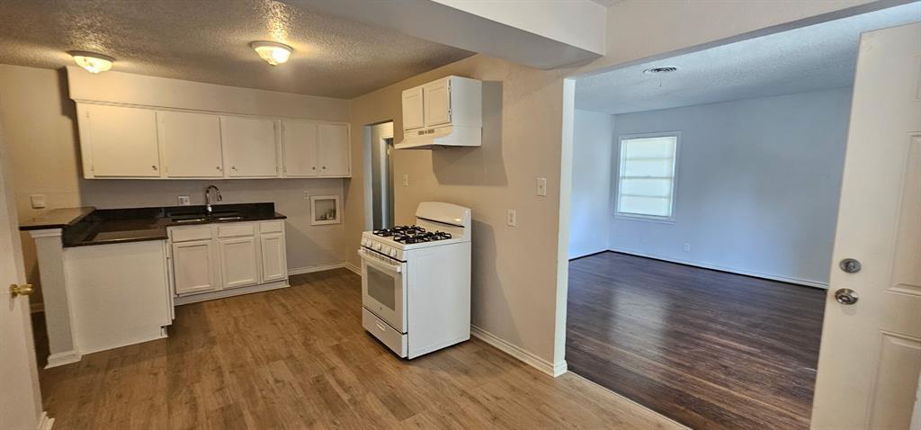 5170 Cardiff Street Dallas, TX 75241 - Photo 7 of 14 Kitchen featuring white gas stove, a textured ceiling, wood finished floors, and white cabinetry