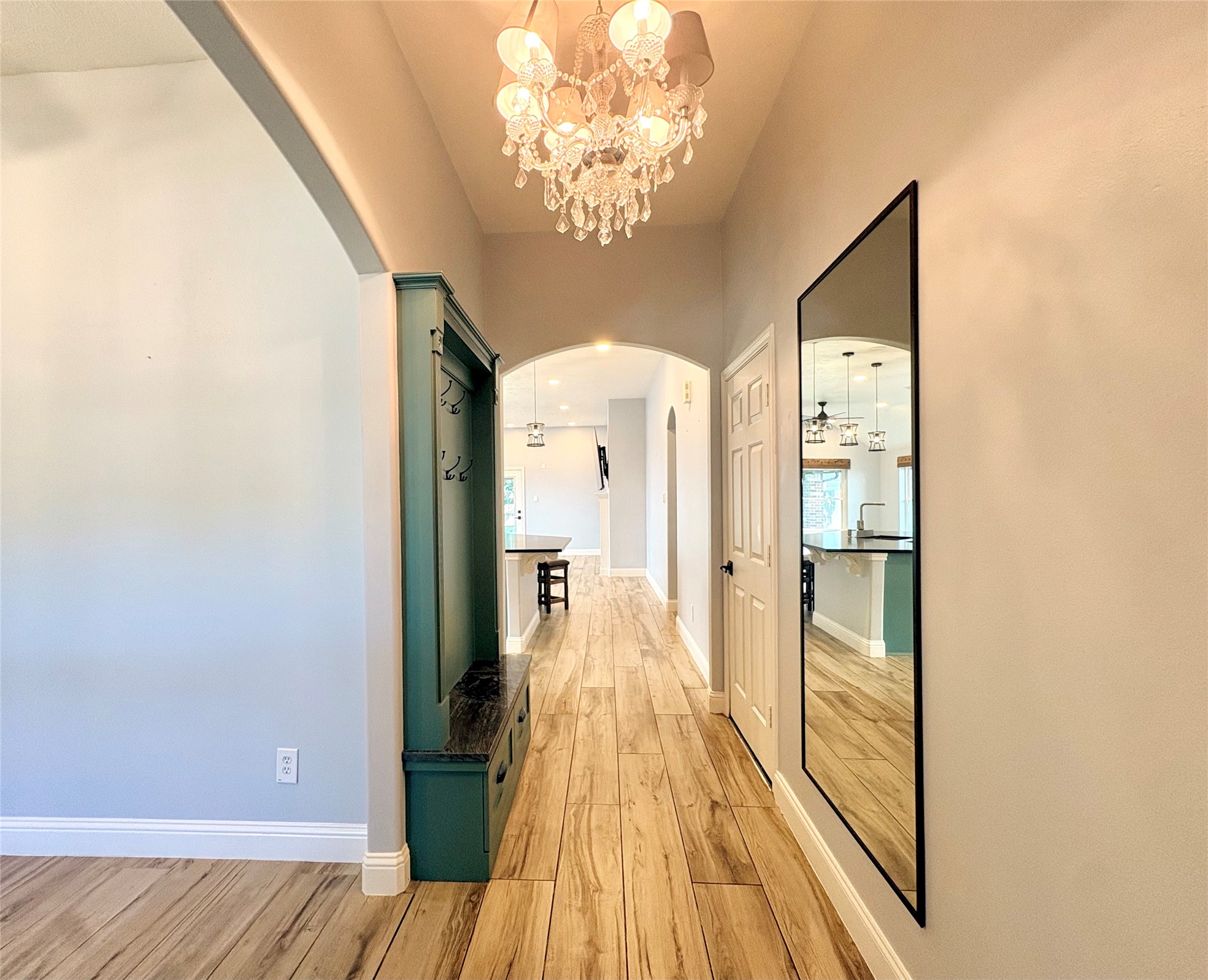 15410 Redbud Berry Way Cypress, TX 77433 - Photo 5 of 49 This image shows a bright, inviting entryway with light wood flooring and a large mirror. A chandelier adds elegance, and an archway leads to an open kitchen area with modern lighting.
