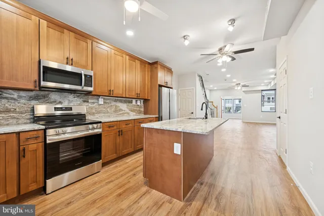 a kitchen with stainless steel appliances granite countertop wooden cabinets a sink dishwasher a stove and a refrigerator with wooden floor