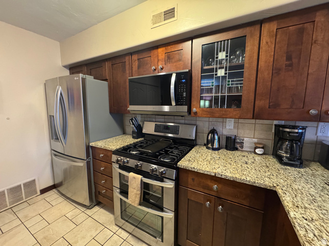 3439 Westwater Road Moab, UT 84532 - Photo 41 of 64 Kitchen with appliances with stainless steel finishes, light stone countertops, decorative backsplash, light tile patterned floors, and dark brown cabinets