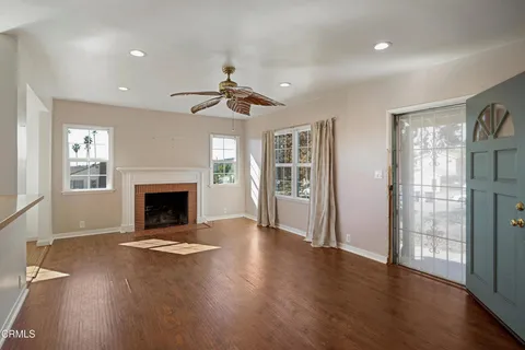 a view of an empty room with wooden floor fireplace and a window