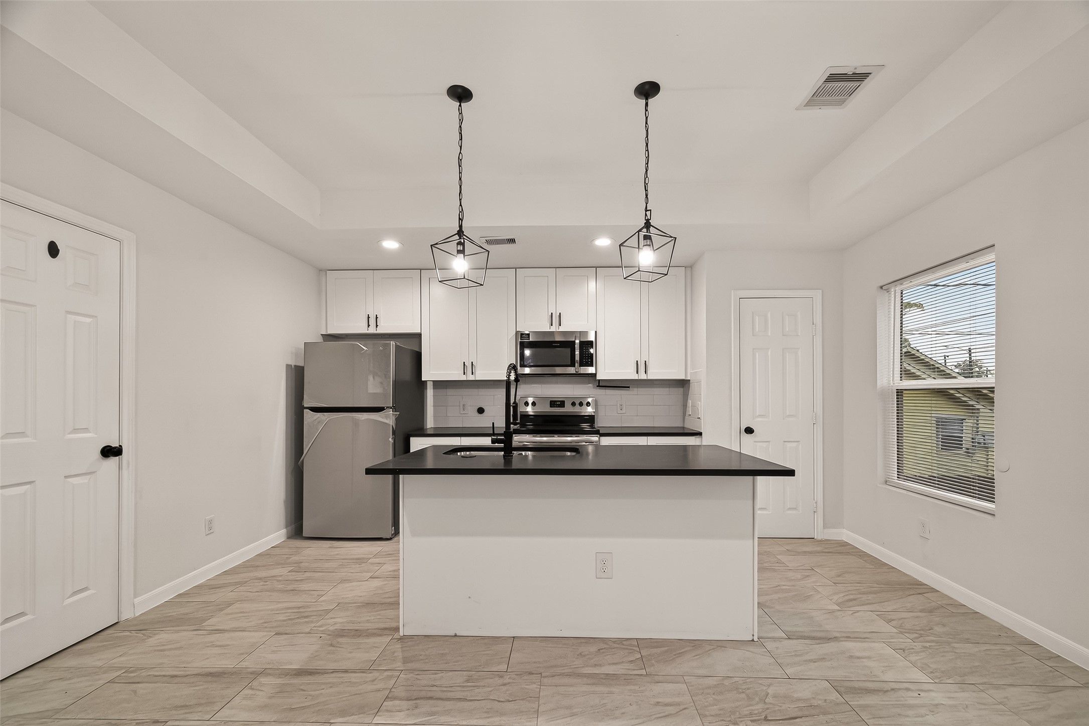4302 Hirsch Road, Unit B Houston, TX 77026 - Photo 2 of 19 Modern kitchen with stainless steel appliances, white cabinetry, and a sleek black countertop island. Features contemporary pendant lighting and a bright, open layout with tiled flooring.