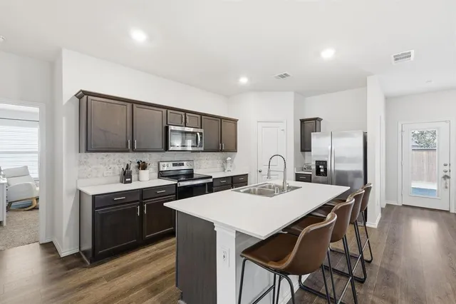 a kitchen with stainless steel appliances a sink a stove a refrigerator cabinets and a dining table