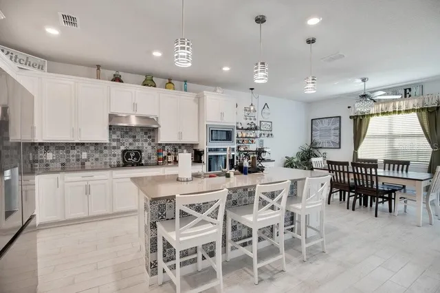a kitchen with stainless steel appliances kitchen island granite countertop a dining table chairs and white cabinets