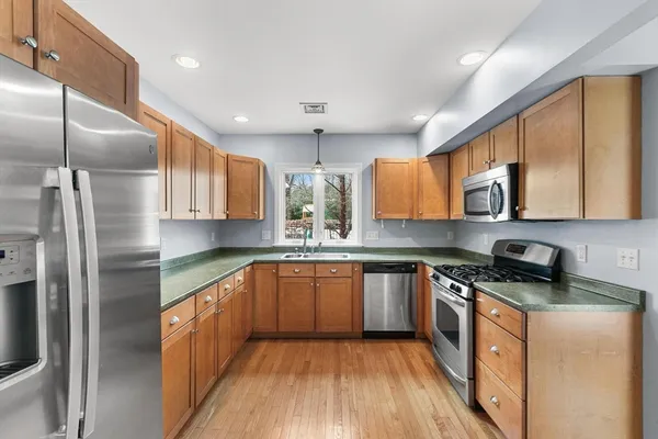 a kitchen with stainless steel appliances granite countertop wooden cabinets a refrigerator a sink a stove a microwave and wooden floors