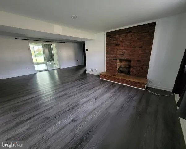 an empty room with wooden floor fire place and windows